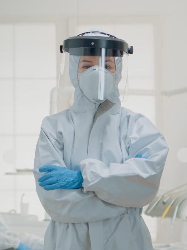 Portrait of dentist standing in hazmat suit for virus protection Portrait of dentist standing in hazmat suit for virus protection at oral clinic. Caucasian woman wearing coverall ppe prepared for dentistry operation and surgical consultation
